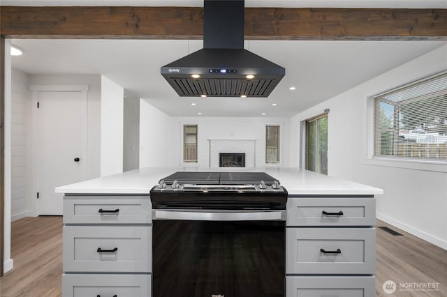 kitchen with light wood-type flooring, gray cabinetry, ventilation hood, stainless steel range with gas cooktop, and light countertops