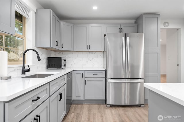 kitchen with gray cabinetry, a sink, tasteful backsplash, stainless steel appliances, and light countertops