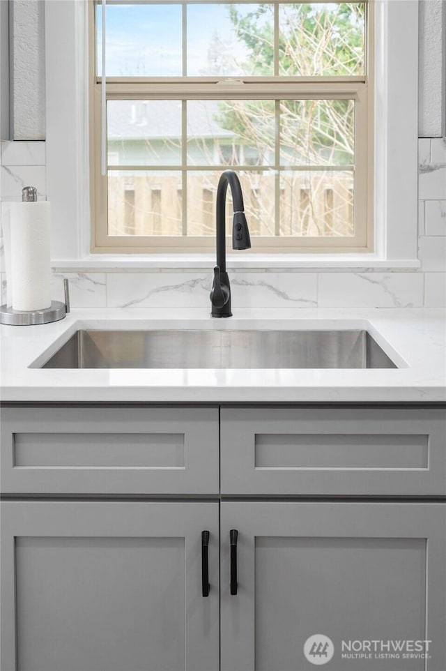 room details featuring decorative backsplash, gray cabinetry, and a sink