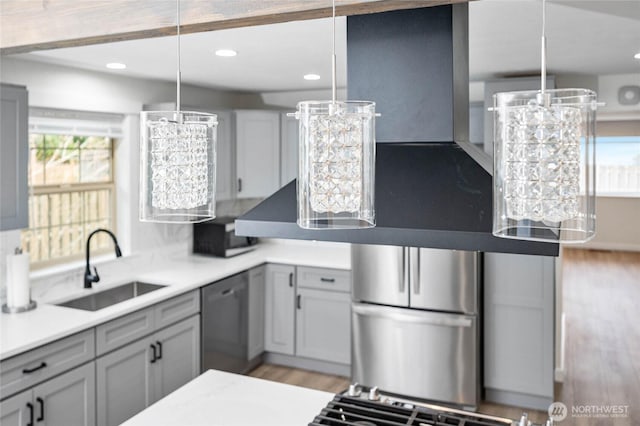 kitchen featuring light wood-type flooring, light countertops, hanging light fixtures, stainless steel appliances, and a sink