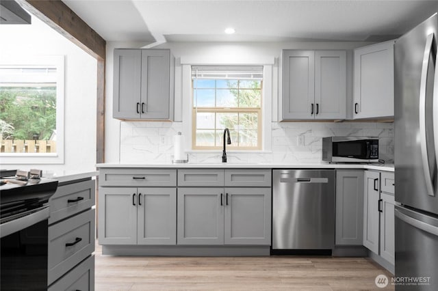 kitchen with light wood finished floors, gray cabinetry, light countertops, stainless steel appliances, and a sink