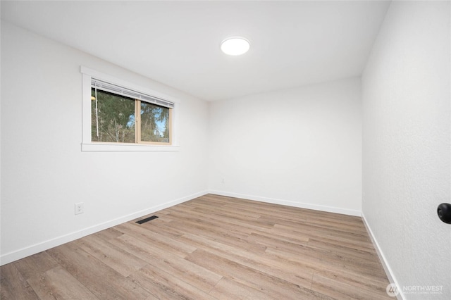 empty room with wood finished floors, visible vents, and baseboards