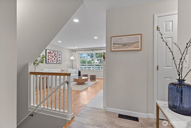 hall featuring light wood finished floors, visible vents, baseboards, an upstairs landing, and recessed lighting