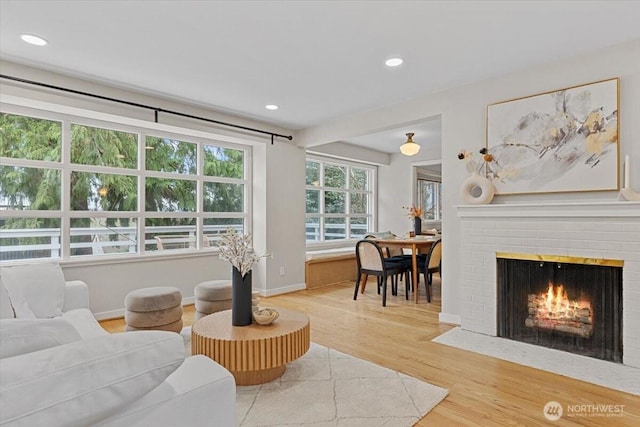 living area featuring recessed lighting, light wood-style flooring, a brick fireplace, and baseboards