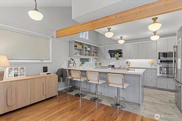 kitchen with a kitchen bar, a sink, lofted ceiling with beams, light wood-style floors, and appliances with stainless steel finishes