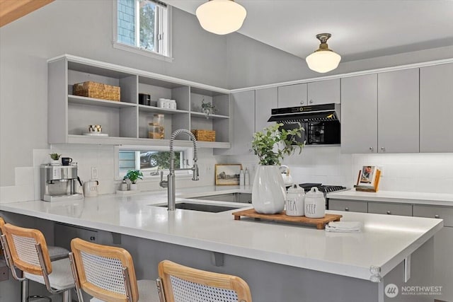 kitchen with a kitchen breakfast bar, gray cabinets, backsplash, and a sink