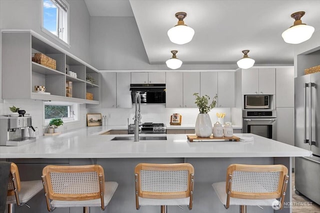 kitchen featuring tasteful backsplash, stainless steel appliances, a peninsula, a breakfast bar area, and light countertops