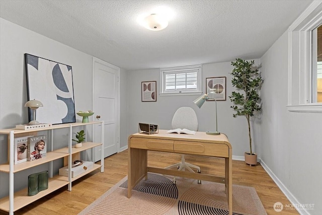 office with light wood-type flooring, baseboards, and a textured ceiling