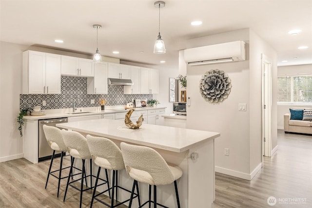 kitchen with a sink, stainless steel appliances, an AC wall unit, under cabinet range hood, and a kitchen breakfast bar