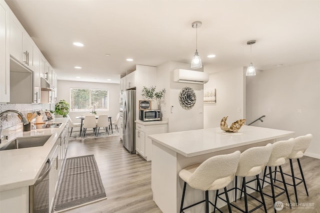 kitchen featuring light wood-type flooring, a wall mounted AC, a sink, a kitchen island, and stainless steel appliances