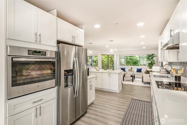 kitchen with backsplash, under cabinet range hood, light countertops, appliances with stainless steel finishes, and a sink