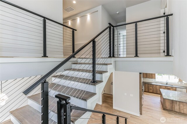 staircase featuring wood finished floors, visible vents, and a towering ceiling