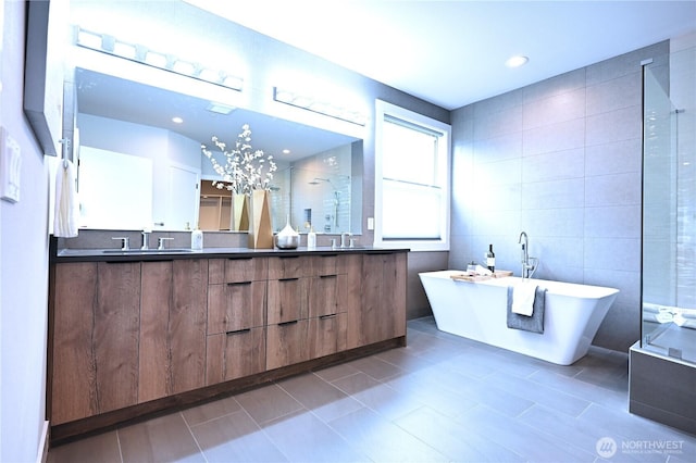 full bath featuring a soaking tub, double vanity, a shower stall, tile walls, and tile patterned floors