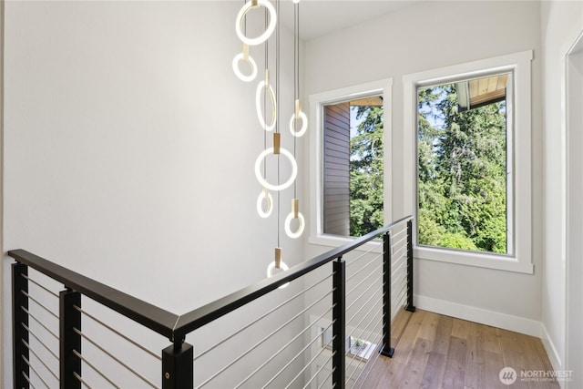 hall featuring baseboards, a healthy amount of sunlight, an upstairs landing, and light wood finished floors