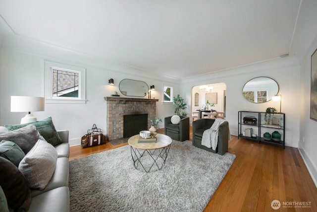 living area with arched walkways, a fireplace, baseboards, and wood finished floors