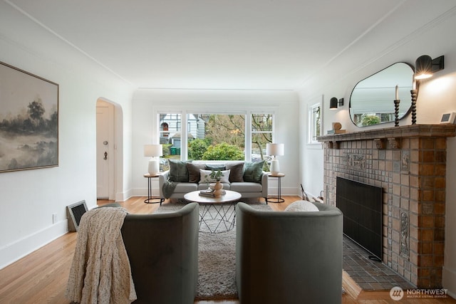 living area featuring a tiled fireplace, wood finished floors, arched walkways, and baseboards