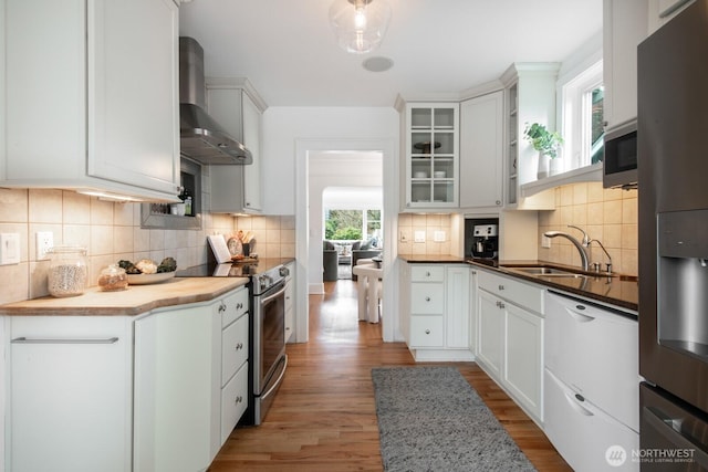 kitchen with a sink, wall chimney range hood, tasteful backsplash, appliances with stainless steel finishes, and light wood finished floors