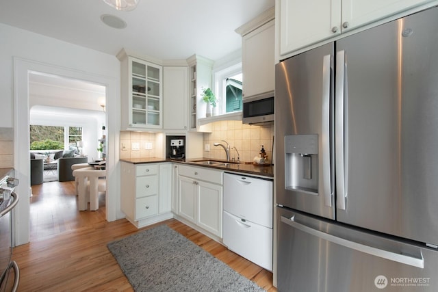 kitchen with tasteful backsplash, dark countertops, light wood-style flooring, appliances with stainless steel finishes, and a sink