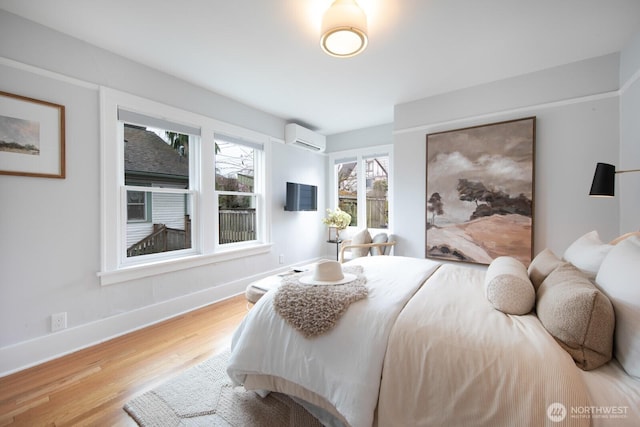 bedroom featuring a wall unit AC, wood finished floors, and baseboards