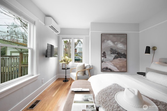 sitting room featuring visible vents, baseboards, an AC wall unit, and wood finished floors