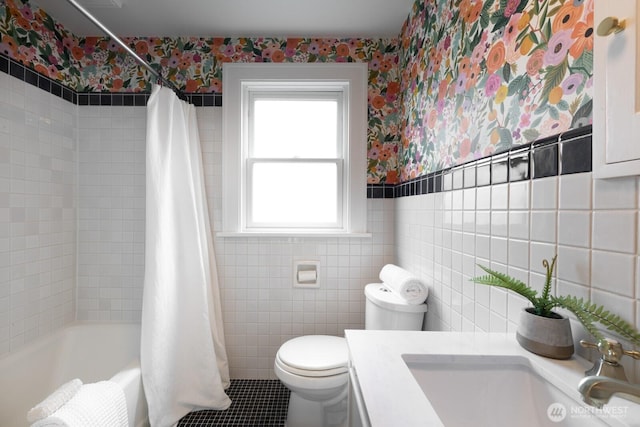 bathroom featuring toilet, tile walls, wainscoting, and wallpapered walls