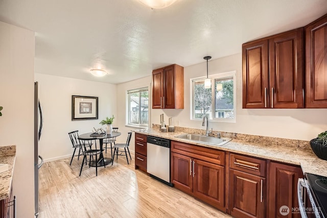 kitchen featuring decorative light fixtures, light wood-style flooring, appliances with stainless steel finishes, brown cabinets, and a sink