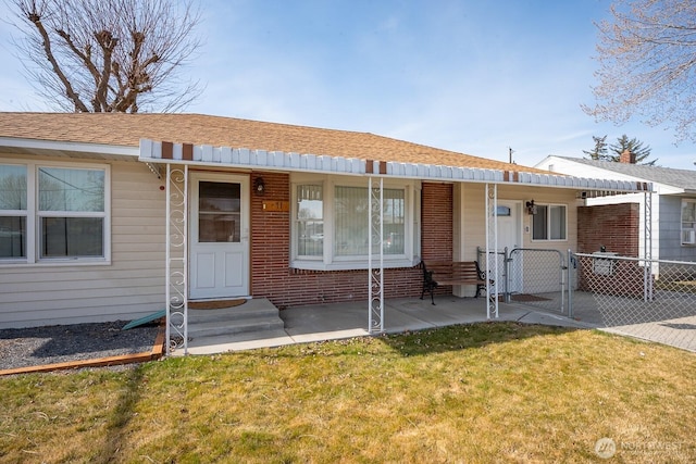 view of front of property featuring a front lawn, a gate, fence, roof with shingles, and brick siding