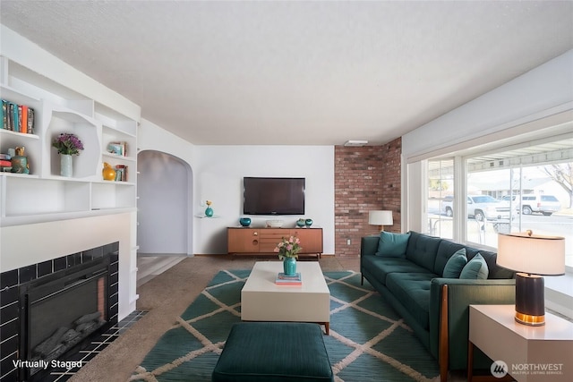 living room featuring a fireplace with flush hearth, arched walkways, and carpet floors