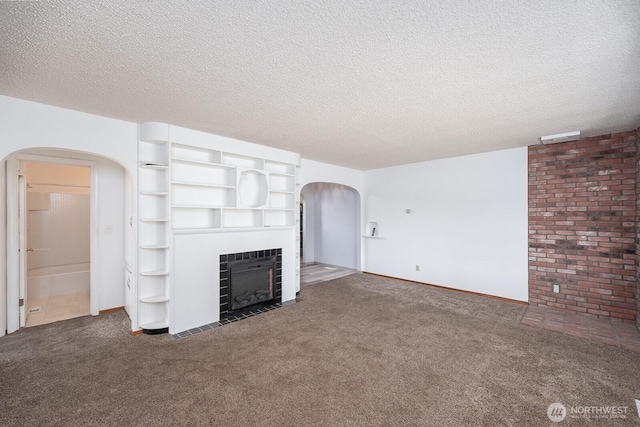 unfurnished living room featuring a tiled fireplace, arched walkways, a textured ceiling, and carpet