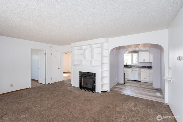 unfurnished living room with a fireplace, arched walkways, a sink, a textured ceiling, and light carpet