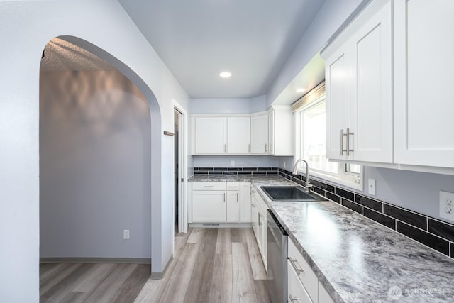 kitchen with a sink, arched walkways, stainless steel dishwasher, and white cabinets