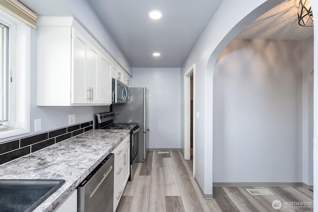 kitchen with recessed lighting, arched walkways, appliances with stainless steel finishes, white cabinets, and light wood finished floors