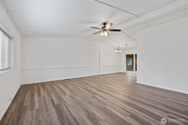 empty room featuring ceiling fan with notable chandelier, lofted ceiling with beams, wood finished floors, and baseboards