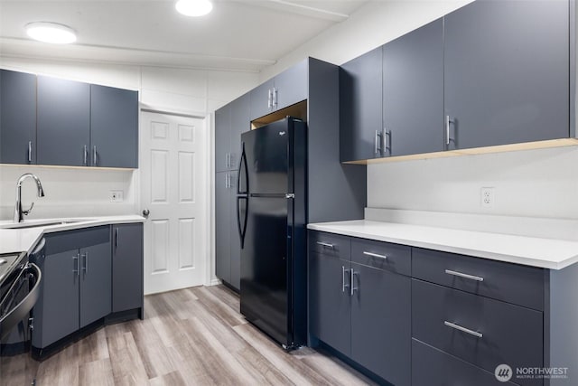 kitchen featuring black appliances, light wood-style floors, light countertops, and a sink