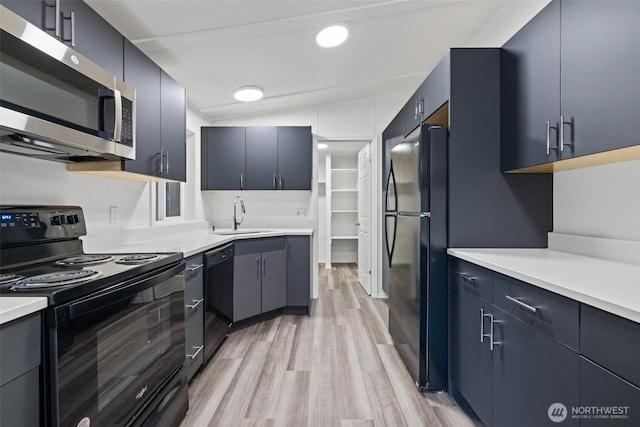 kitchen featuring black appliances, light countertops, light wood finished floors, and a sink