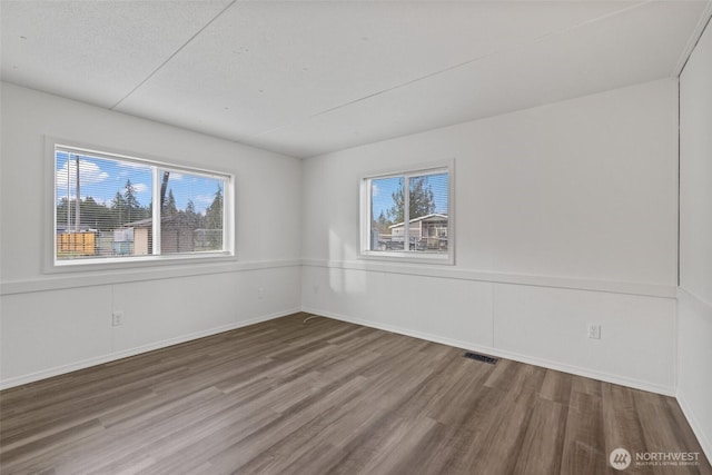 spare room with wood finished floors, visible vents, and baseboards