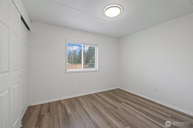 unfurnished bedroom featuring a closet, crown molding, baseboards, and wood finished floors