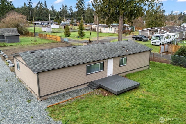 rear view of property featuring a lawn, a deck, fence, a residential view, and a shingled roof