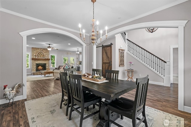 dining space featuring arched walkways, a fireplace, wood finished floors, ceiling fan with notable chandelier, and ornamental molding