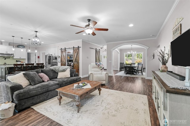 living room with arched walkways, ceiling fan with notable chandelier, a barn door, and dark wood-type flooring
