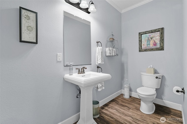 half bathroom with baseboards, ornamental molding, toilet, and wood finished floors