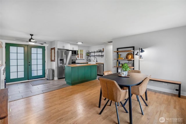 dining space featuring light wood-style flooring, french doors, a ceiling fan, and baseboards