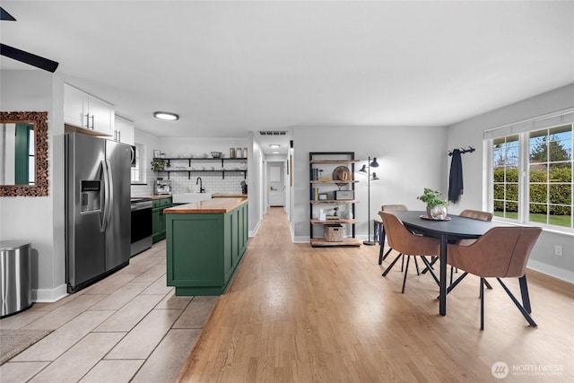 kitchen with backsplash, green cabinets, butcher block countertops, stainless steel appliances, and open shelves