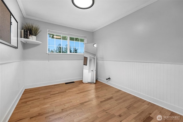 unfurnished room with visible vents, ornamental molding, a wainscoted wall, and wood finished floors