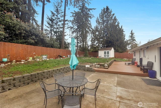 view of patio / terrace with a wooden deck, outdoor dining area, a fenced backyard, an outdoor structure, and a storage shed