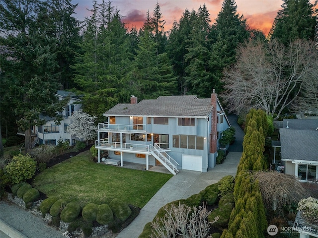 view of front of home featuring driveway, a front lawn, stairway, an attached garage, and a chimney