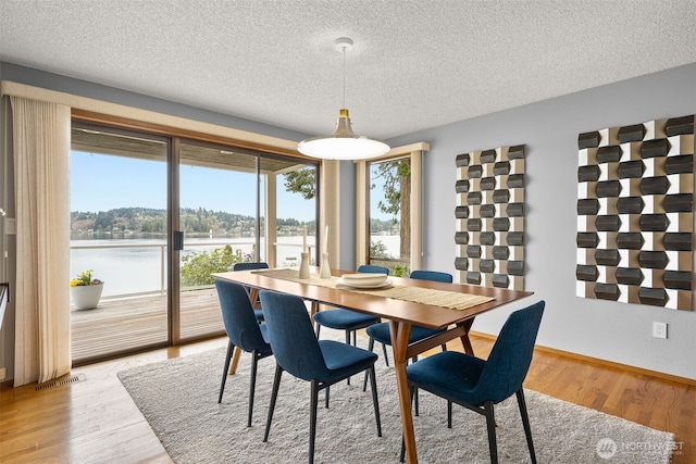 dining space with a water view, visible vents, light wood finished floors, and a textured ceiling