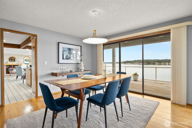 dining area with visible vents, light wood-style flooring, a textured ceiling, and a water view