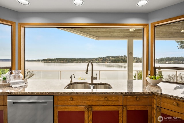 kitchen with a sink, a water view, stainless steel dishwasher, and brown cabinetry