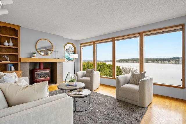 living area with a textured ceiling, wood finished floors, a water view, and a tile fireplace